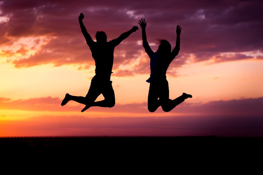 Silhouette of engaged couple jumping on the beach at sunset