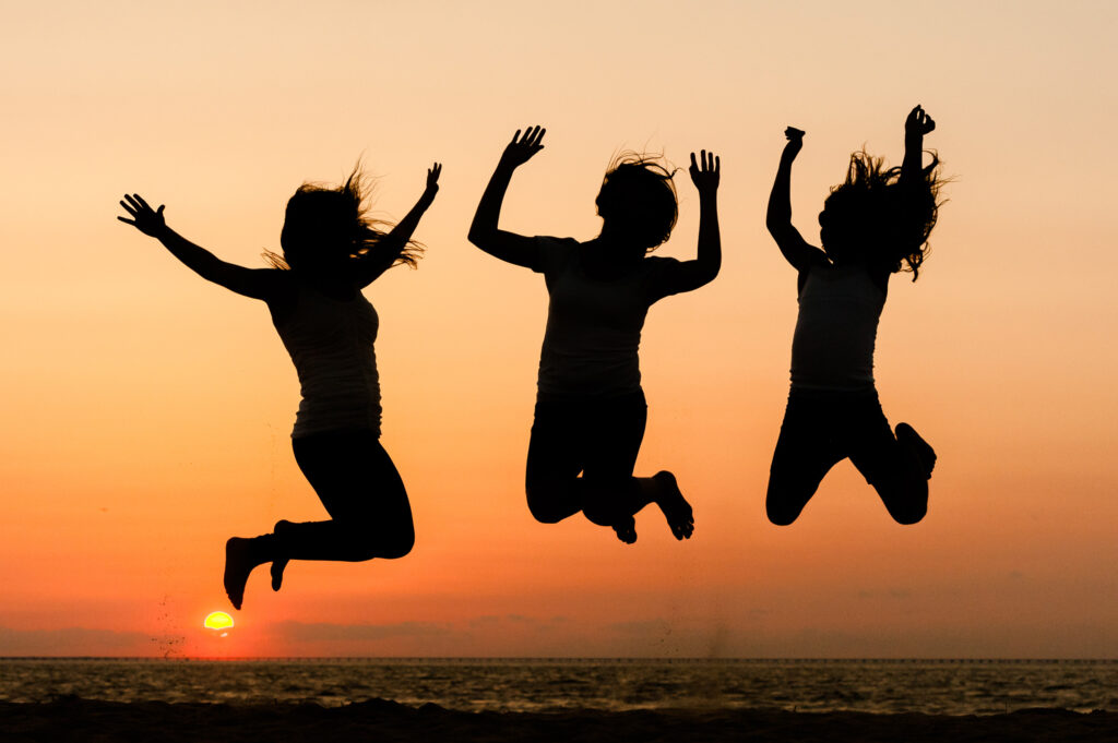 Three sisters jumping on the beach at sunset in silhouette