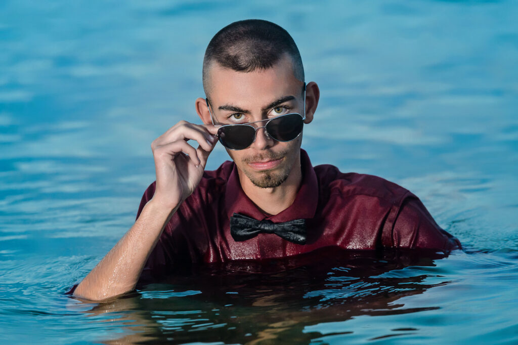 Abstract senior portrait of a young man coming out of the water with his sunglasses on