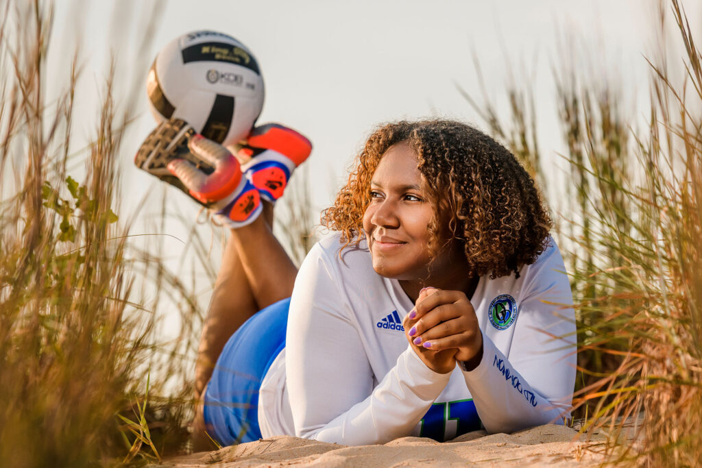 Young girl at her senior portrait session dressed in her volleyball uniform with a volleyball on her feet